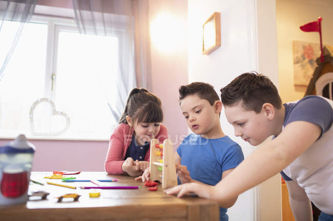Menino com Síndrome de Down e irmãos brincando com brinquedos na mesa — Fotografia de Stock