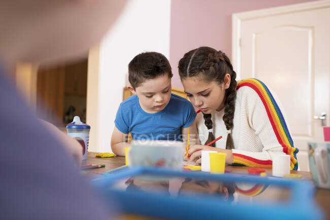 Мальчик с синдромом Дауна и сестра раскраски за столом — стоковое фото