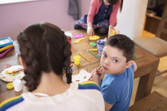 Retrato lindo niño con síndrome de Down para colorear en la mesa con hermanos - foto de stock