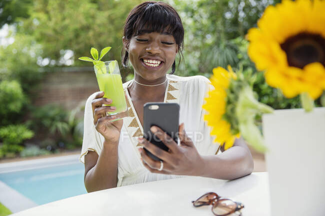 Happy young woman drinking cocktail and video chatting at poolside — Stock Photo