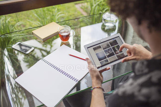 Young man looking at photographs on digital tablet in home office — Stock Photo