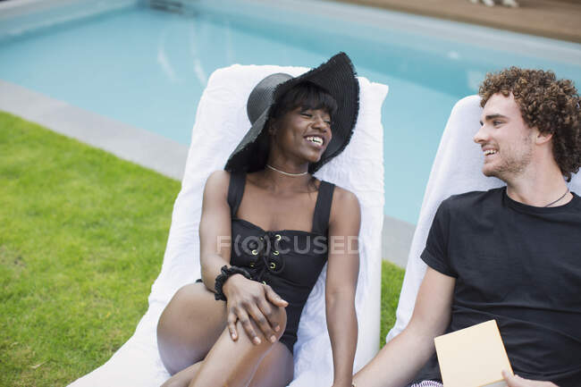 Счастливая молодая пара отдыхает в шезлонгах у бассейна — стоковое фото