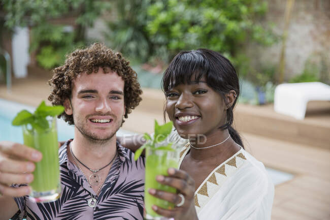 Портрет щаслива багатонаціональна молода пара п'є коктейлі біля басейну — стокове фото