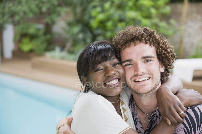 Portrait happy young multiethnic couple hugging at poolside — Stock Photo
