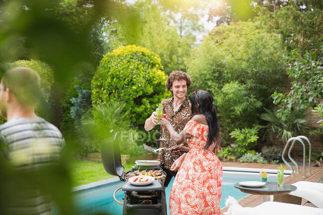 Young multiethnic couple toasting cocktails at poolside barbecue grill — Stock Photo