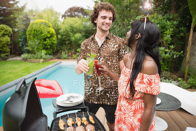 Joyeux jeune couple qui boit des cocktails au barbecue de la piscine — Photo de stock