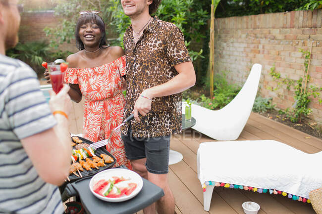 Happy young multiethnic couple barbecuing on summer patio — Stock Photo