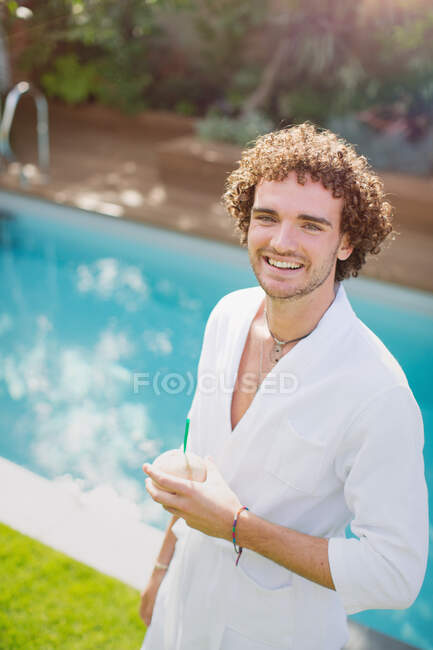 Retrato joven feliz en albornoz bebiendo de coco en la piscina - foto de stock