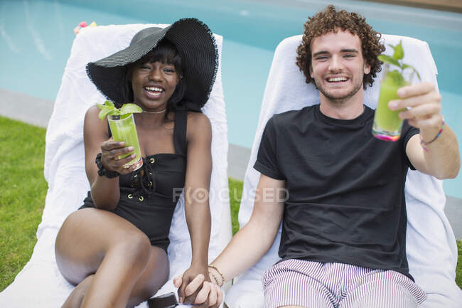 Портрет щаслива молода багатоетнічна пара п'є коктейлі біля басейну — стокове фото