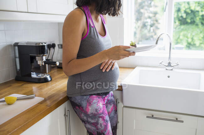 Pregnant woman eating in kitchen — Stock Photo