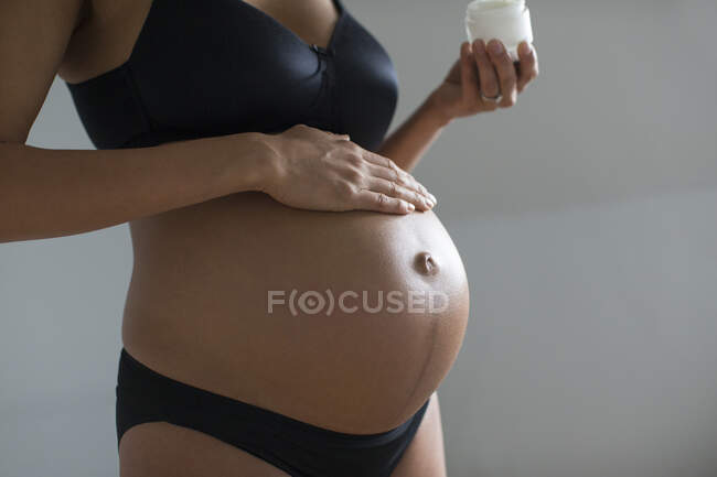 Закройте беременную женщину, нанося увлажняющий крем на живот — стоковое фото