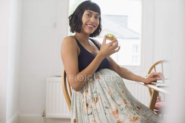 Retrato feliz mujer embarazada comiendo tostadas de aguacate - foto de stock