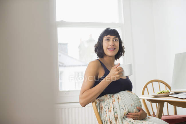 Beautiful pregnant woman drinking tea at dining table — Stock Photo