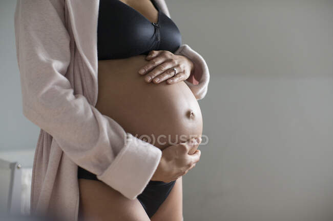 Pregnant woman in bra and panties holding stomach — Stock Photo