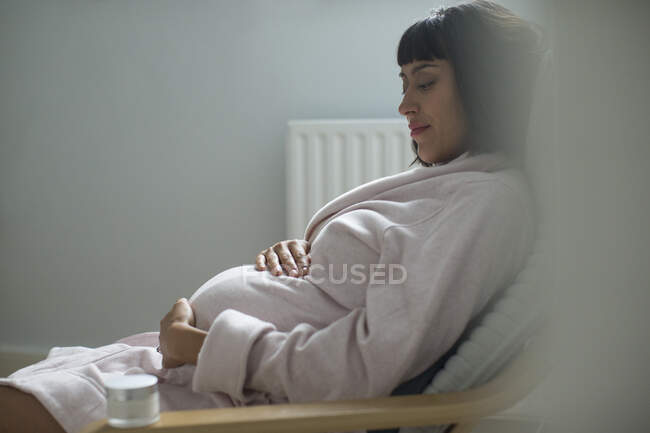 Serene pregnant woman in bathrobe holding stomach — Stock Photo