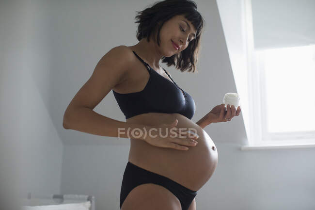 Pregnant woman in bra and panties applying moisturizer to stomach — Stock Photo