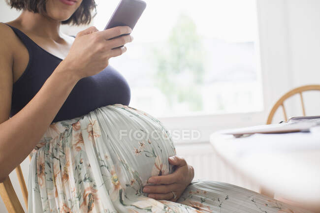 Mulher grávida em vestido floral usando telefone inteligente — Fotografia de Stock