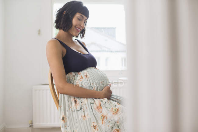 Felice donna incinta in abito floreale che tiene lo stomaco — Foto stock