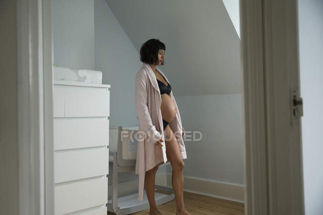 Serene pregnant woman in bathrobe standing in baby nursery — Stock Photo
