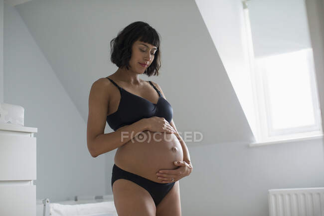 Serena mulher grávida em sutiã e calcinha segurando estômago — Fotografia de Stock