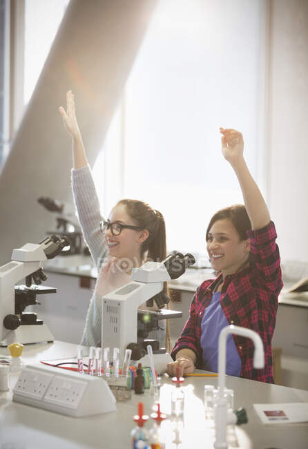 Alunos ansiosos levantando os braços atrás de microscópios em sala de aula de laboratório — Fotografia de Stock