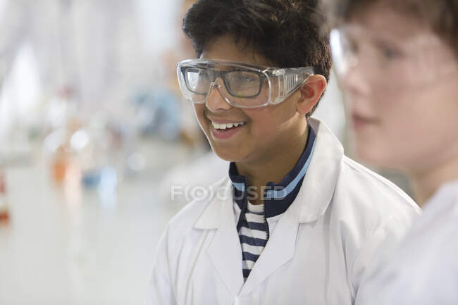 Garoto sorridente vestindo óculos e jaleco em sala de aula de laboratório — Fotografia de Stock