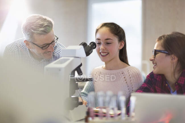 Чоловічий вчитель і студенти-дівчата проводять науковий експеримент в мікроскопі в лабораторному класі — стокове фото