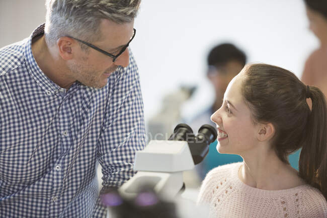 Male teacher and smiling girl student conducting scientific experiment at microscope in laboratory classroom — Stock Photo