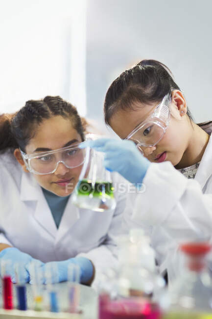 Estudiantes examinando líquido en vaso de precipitados, realizando experimentos científicos en el aula de laboratorio - foto de stock
