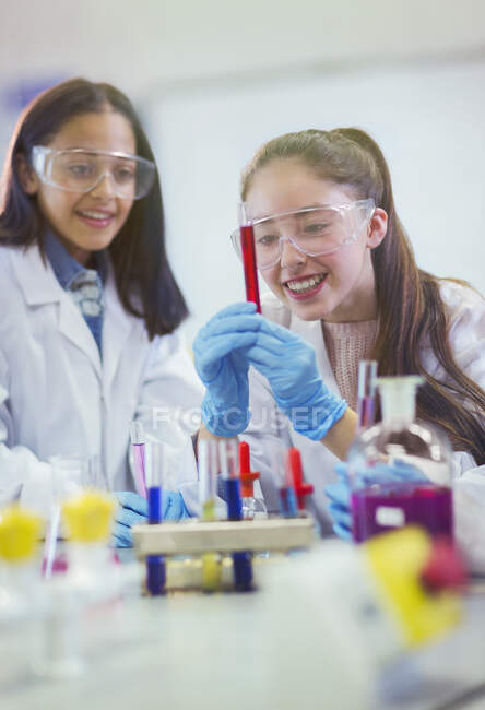 Estudiantes sonrientes examinando líquido en tubo de ensayo, realizando experimentos científicos en aula de laboratorio - foto de stock