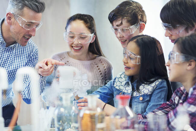 Учитель и ученики мужского пола наблюдают за химической реакцией, проводят научные эксперименты в лабораторном классе — стоковое фото