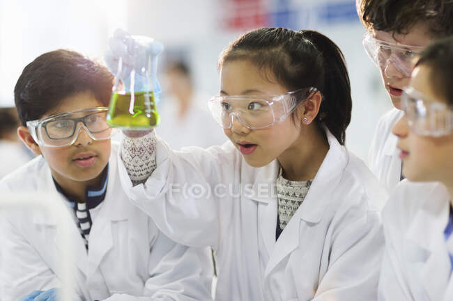 Estudiantes curiosos examinando líquido en vaso de precipitados, llevando a cabo experimentos científicos en el aula de laboratorio - foto de stock