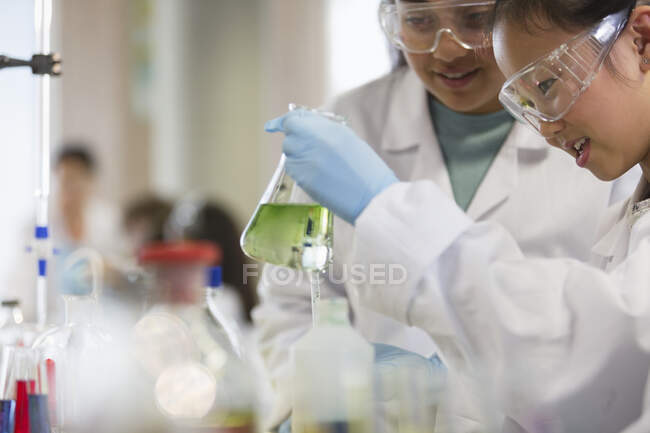Студенти-дівчата проводять науковий експеримент, вивчаючи рідину в склянці в лабораторному класі — стокове фото