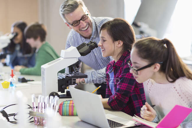 Усміхнений вчитель чоловічої науки допомагає студентам-дівчатам проводити науковий експеримент на мікроскопі в лабораторії — стокове фото