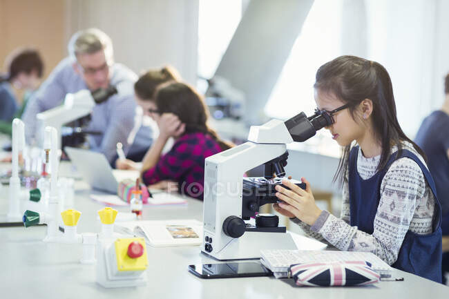 Girl student using microscope, conducting scientific experiment in laboratory classroom — Stock Photo