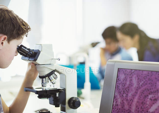 Мальчик-ученик с помощью микроскопа проводит научный эксперимент в лабораторном классе — стоковое фото