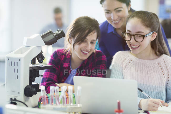 Female teacher and girl students using microscope and laptop, conducting scientific experiment in laboratory classroom — Stock Photo