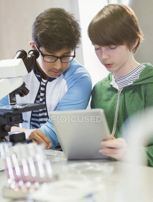 Студенти, орієнтовані на хлопчика, використовують цифровий планшет і мікроскоп, проводять науковий експеримент в лабораторному класі — стокове фото