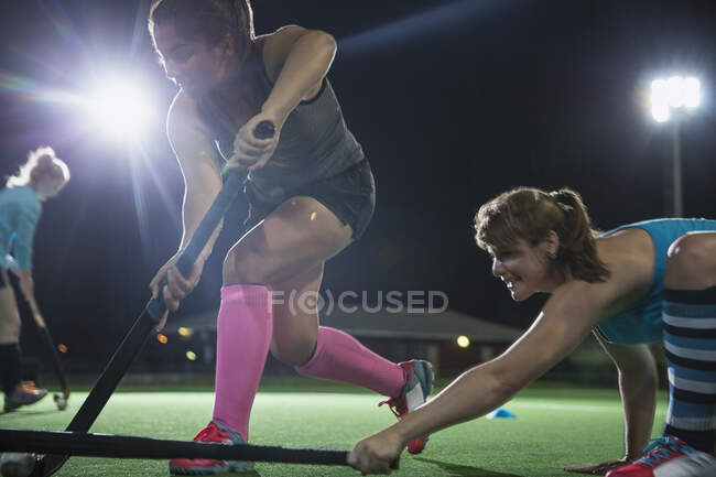 Решительные женщины хоккеисты на траве играют, достигая с хоккейными клюшками — стоковое фото