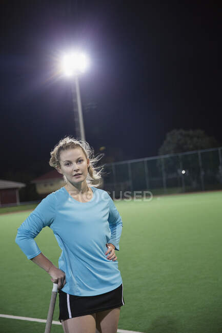 Ritratto serio giovane giocatore di hockey su prato femminile sul campo di notte — Foto stock
