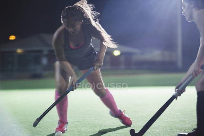 Решительная молодая женщина хоккеистка достигает с хоккейной клюшкой, играя на поле ночью — стоковое фото