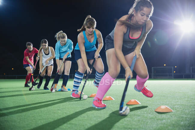Determinadas jugadoras de hockey sobre hierba practicando ejercicios deportivos en el campo por la noche - foto de stock