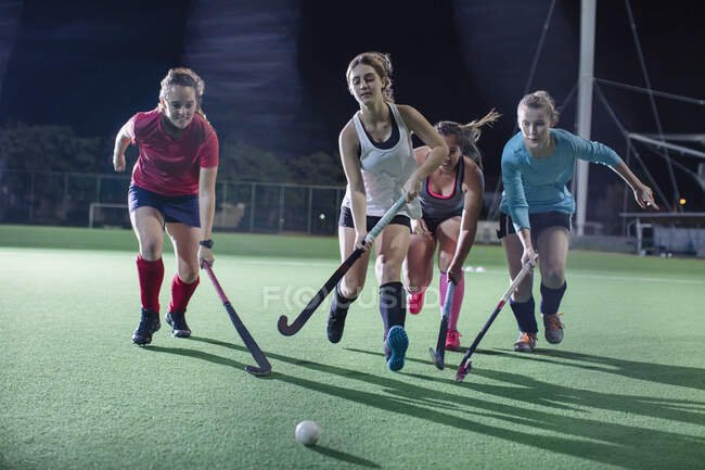 Young female field hockey players running for the ball, playing on field at night — Stock Photo