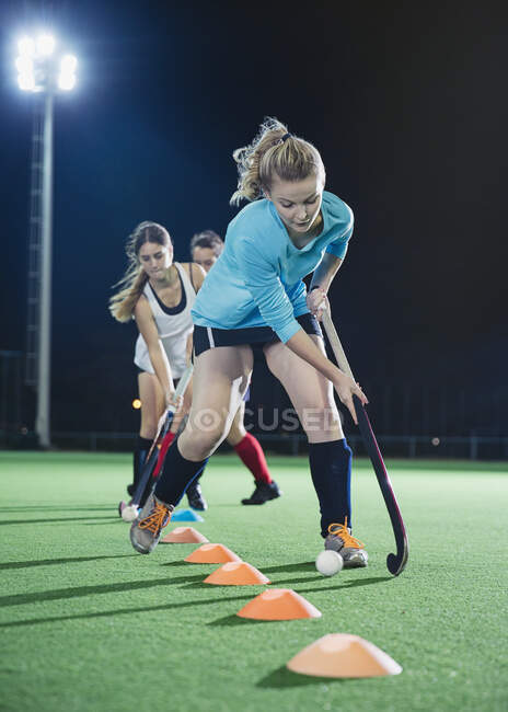 Determinada joven jugadora de hockey sobre hierba practicando ejercicios deportivos en el campo por la noche - foto de stock
