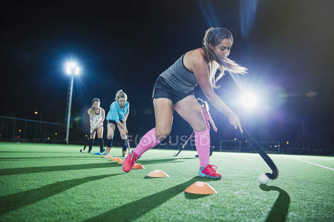 Determinada joven jugadora de hockey sobre hierba practicando ejercicios deportivos en el campo por la noche - foto de stock