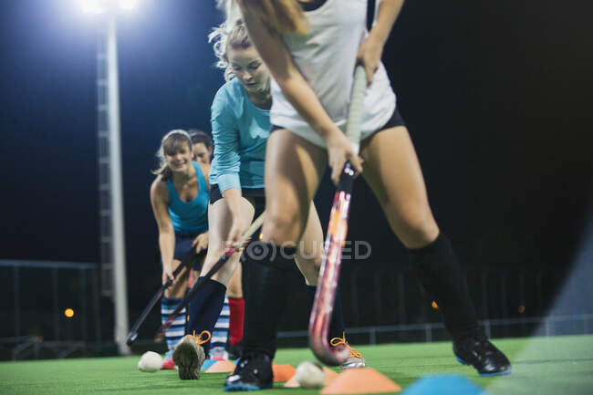 Determinadas jóvenes jugadoras de hockey sobre hierba practicando ejercicios deportivos en el campo por la noche - foto de stock