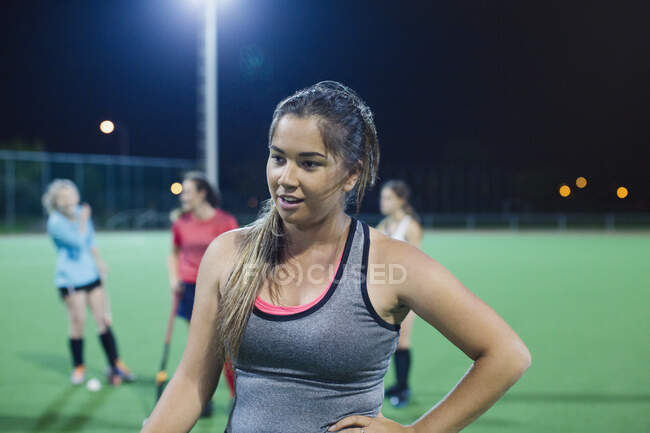 Tired young female field hockey player resting on field at night — Stock Photo