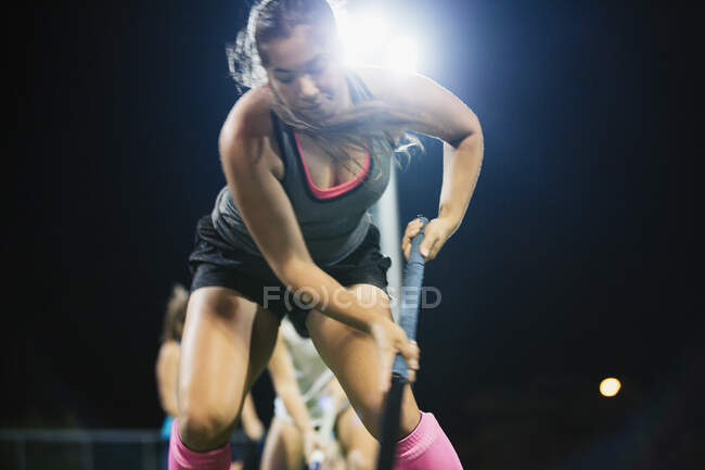 Determined young female field hockey player practicing sports drill at night — Stock Photo