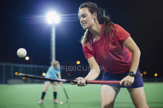 Young female field hockey player bouncing ball off hockey stick, practicing on field at night — Stock Photo