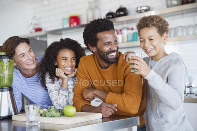 Мультиэтническая семья делает и пьет здоровый зеленый смузи на кухне — стоковое фото